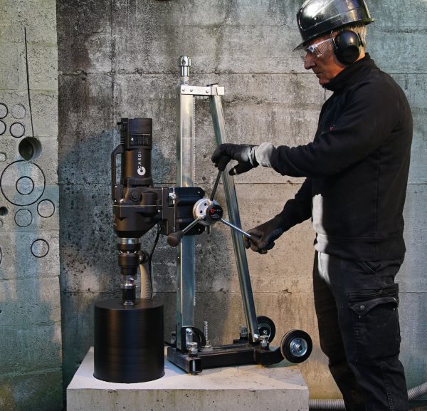 Construction worker drill concrete with CARDI HS 300 core drill with core bit on stand.