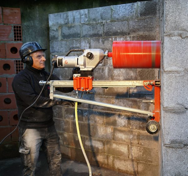 Construction worker drill a wall with CARDI 500 core drill on stand with core bit.