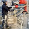 Construction worker drill a wall with CARDI 500 core drill on stand with core bit.